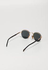 Ochelari de soare rotunzi cu lentile întunecate, cadru din metal de aur și brațe din plastic negru. Prezintă un design simplu, fără modele sau accente suplimentare.