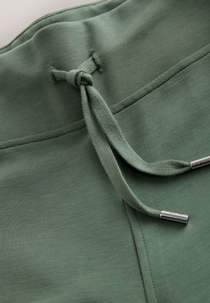 Zielona tkanina z mieszanki bawełny z zamkiem ściągającym zakończonym srebrnymi końcówkami. Gładka tekstura i wykończone krawędzie, zaprojektowane dla komfortu.