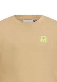 Beżowy bawełniany t-shirt z okrągłym dekoltem. Posiada małe żółto-zielone logo "RETOUR R" na górnej lewej stronie. Gładka tekstura.