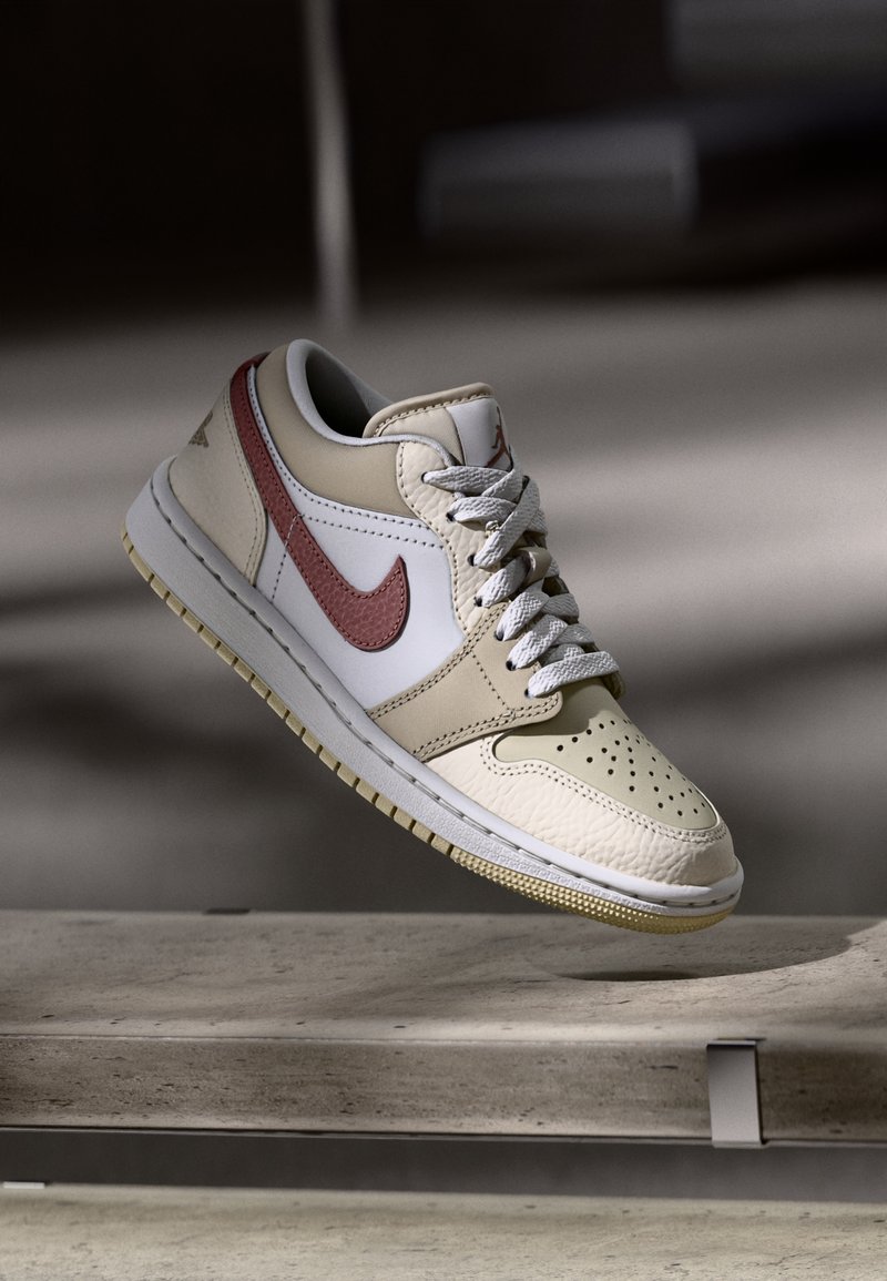 Sneakers in pelle beige e bianca con swoosh rosso, punta tonda e dettagli testurizzati. Allacciate con lacci grigio chiaro e con un discreto dettaglio del logo.