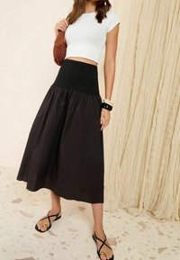 Mustat, polvipituiset hameet, joissa on poimutettu muotoilu ja joustava vyötärö; yhdistettynä valkoiseen lyhytlahkeiseen toppiin ja mustiin nilkkaketjullisiin sandaaleihin.