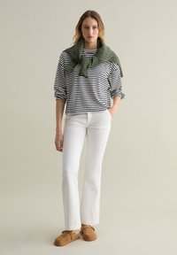 Maglione di cotone a righe con sciarpa di lana verde, jeans bianchi a zampa d'elefante e zoccoli in suede marrone. Design semplice con vestibilità casual e texture.