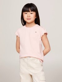 Vaaleanpunainen lyhythihainen t-paita, jossa röyhelöreunat, yhdistetty kermaan vivahtaviin cargo-shortseihin, joissa on taskut ja hienovaraiset ompelukoristeet.