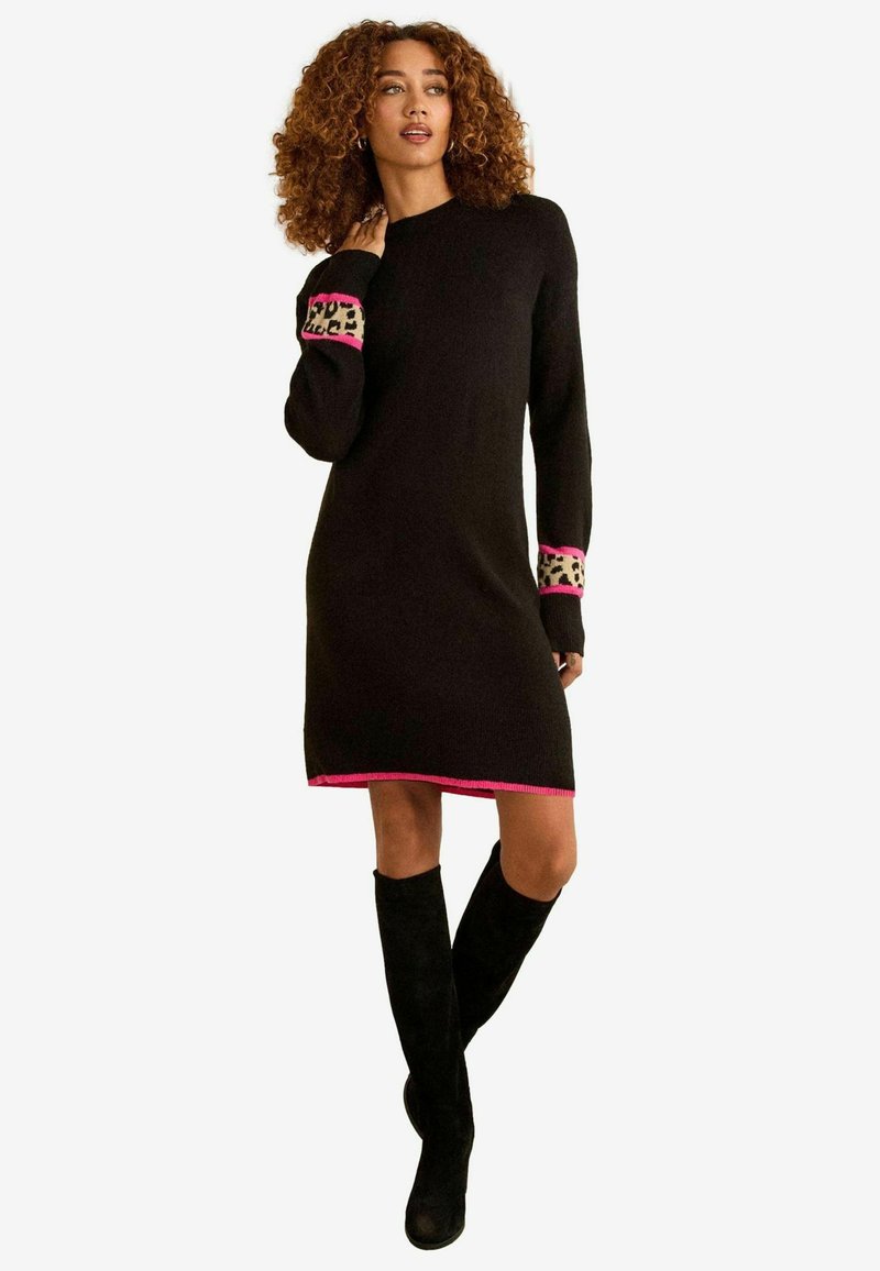 Abito nero lavorato a maglia con taglio dritto, caratterizzato da dettagli rosa e stampa leopardata sui polsini. Indossato con stivali neri al ginocchio.