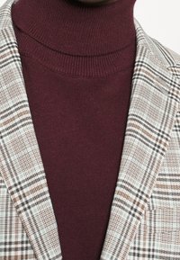 Geruite blazer in beige, zwart en bruin met een donker bordeauxrood coltrui. Gestructureerde breiselstof, getailleerde pasvorm, contrasterende kleuren.