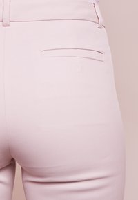 Jasnoróżowe spodnie o gładkiej teksturze, z ukrytym wzorem kieszeni z tyłu i dopasowanym fasonem w talii.