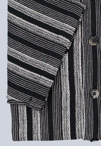 Schwarz-weiß gestreiftes Hemd mit gewebter Textur, Knopfverschluss und umgeschlagenen Ärmeln. Die Streifen variieren in Breite und Muster.