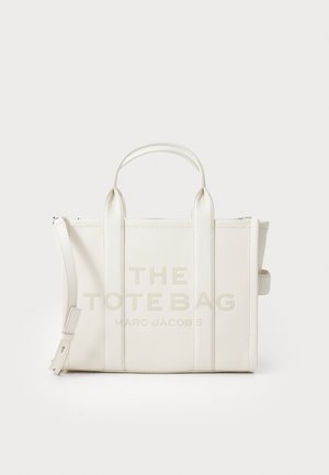 Weiße Leder-Tote mit doppelten Obergriffen, mit bedrucktem Text "DER TOTE BAG MARC JACOBS" und Reißverschlussverschluss. Glatte Textur, rechteckige Form.