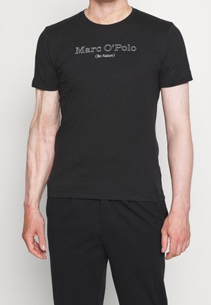 Homme portant un t-shirt noir à manches courtes et un pantalon noir, le texte sur le t-shirt indique "Marc O'Polo (Re-Nature)" en lettres blanches.