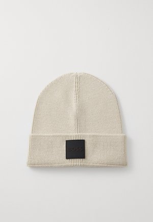 Beige kötött sapka hajtott szegéllyel, fekete bőr téglalap alakú címkével, amelyen a "BOSS" felirat van domborítva. Simma textúra, klasszikus dizájn.