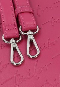 Détail d'un sac en cuir rose fluo présentant de la quincaillerie argentée brillante et deux clips détachables, embossés d'un motif de nom de marque.