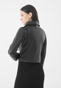 Zwarte leren jas met een cropped ontwerp, hoge kraag en een textuurafwerking. Inclusief accentstiksels en metalen hardwaredetails.
