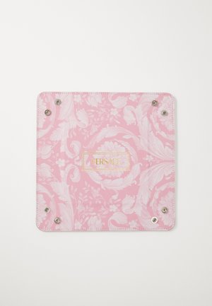 Pink patterned accessory with floral design, featuring metallic snap fasteners and a gold "VERSACE" logo on a textured surface.