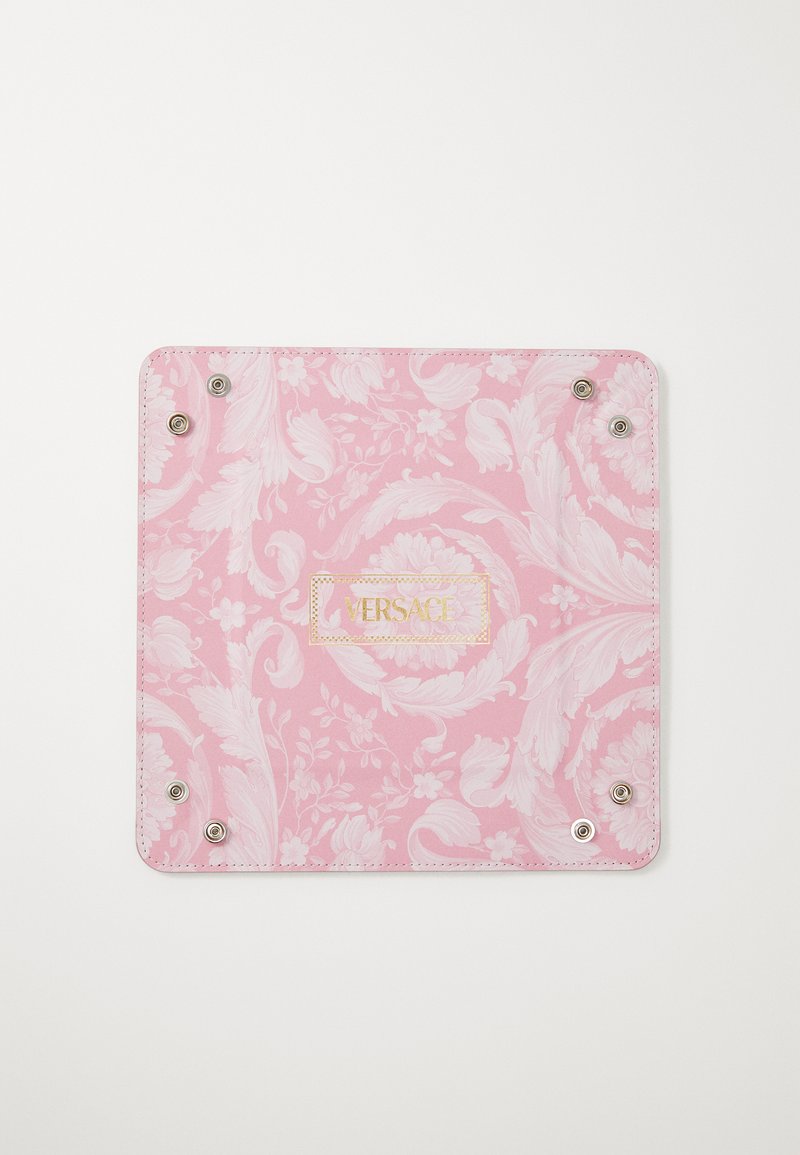 Ροζ αξεσουάρ με σχέδιο λουλουδιών, που διαθέτει μεταλλικά κουμπώματα και χρυσό λογότυπο "VERSACE" σε υφή επιφάνειας.