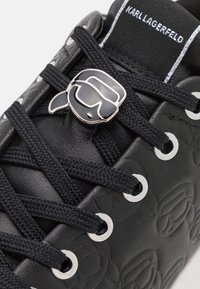 Sneaker nera in pelle con dettagli testurizzati, lacci neri, occhielli argentati e un logo lucido di Karl Lagerfeld sulla linguetta.