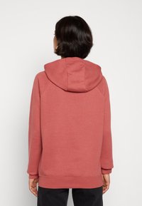 Hoodie i dammrosa färg med avslappnad passform, ribbstickade muddar och mjuk textur, sedd bakifrån.