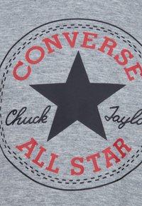 Gray fabric featuring a circular logo with a black star. Text includes "CONVERSE" and "ALL STAR" in red, with "Chuck Taylor" in black script.