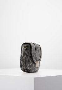 Crossbody kabelka s hadím vzorem v černé a šedé barvě, s překlápěcí klopou a kovovým kováním, má texturovaný povrch a zaoblený tvar.
