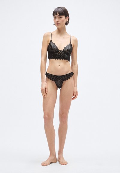 Čierny čipkovaný bralet a zodpovedajúce nohavičky s diamantovým vzorom. Bralet má tenké ramienka a vlnité okraje. Hladká textúra.