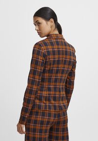 Brun og marineblå plaid blazer med en tætsiddende design, smalle revers og lange ærmer, der har diskrete pink accenter i mønsteret.
