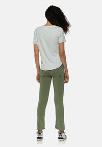 Camiseta de manga corta gris claro combinada con pantalones ajustados verde oliva. Los pantalones tienen un dobladillo acampanado y detalles desgastados en la parte inferior.