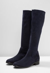 Stivali blu navy al ginocchio realizzati in morbido suede, caratterizzati da un design elegante e un tacco basso e impilato per una maggiore stabilità.