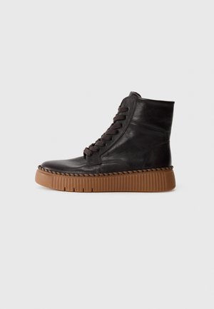Zapatillas altas de cuero negro con suela de plataforma de goma marrón, que presentan cordones en tono y detalles cosidos a lo largo de la suela.