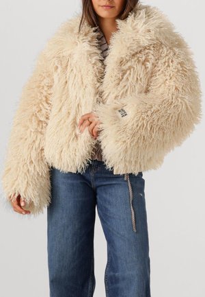 Faux fur jacket in cream with a fluffy texture, oversized sleeves, and a tag on the cuff. Paired with blue jeans.