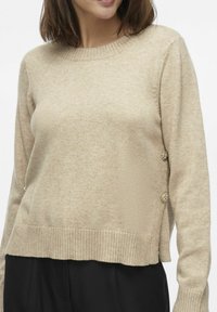 Beige kootud särk ribitud äärisega, ümmarguse kaelusega ja dekoratiivsete nuppudega külgedel. Pehme tekstuur, mugav lõige ja lühike pikkus.