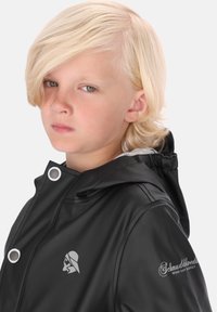 Melna ūdensnecaurlaidīga jakas ar kapuci, ar pelēkiem akcentiem un logotipu uz krūtīm. Gluda tekstūra ar snap pogām un acu detaļām.