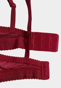 Burgundy bra strap with adjustable hooks and textured fabric. Features scalloped edges, elastic bands, and a three-hook closure in back.