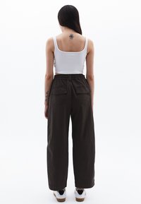 Witte tanktop en donkerbruine wijde broek met elastische tailleband, met twee achterzakken, gecombineerd met witte sneakers.