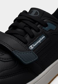 Μαύρο αθλητικό παπούτσι με δερμάτινο επάνω μέρος, διακοσμητικές τρύπες, χοντρές κορδόνια, ρυθμιζόμενο λουράκι και αντιθετική επωνυμία. Λευκή σόλα με υφή για καλύτερη πρόσφυση.