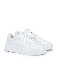 White leather sneakers with perforated details, flat laces, a thick white sole, and subtle gold accents on the tongue and side.