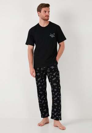 Sort bomulds T-shirt med en hvid UFO-grafik på brystet, parret med sorte pyjamasbukser med et rum-tema mønster i hvidt.