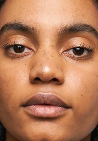 Close-up van een gezicht met bruine ogen, volle lippen en een gladde huidtextuur met sproetjes. Natuurlijke make-up accentueert de kenmerken.
