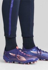 Fialové futbalové kopačky s textúrovaným dizajnom, s ružovými akcentmi a čiernymi šnúrkami. Športový vzhľad s nízkym strihom pre obratnosť.