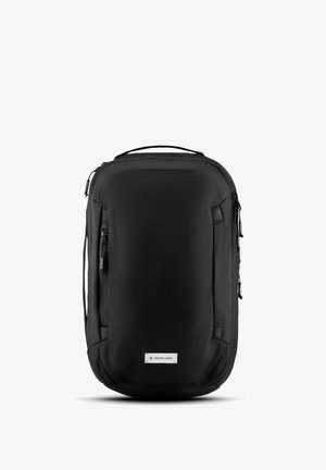 Sac à dos en tissu noir au design épuré, équipé de zips, de poches latérales et d'une étiquette de marque au centre en bas.