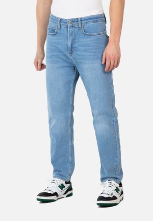 Hellblaue Jeans aus Denim mit geradem Schnitt, fünf Taschen und einer Metallknopfverschluss. Getragen mit schwarz-weißen Sneakers.