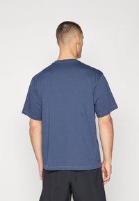 Tricou din bumbac bleumarin, cu mâneci scurte, guler rotund și un mic logo pe spate. Prezintă cusături la margini și o croială lejeră.