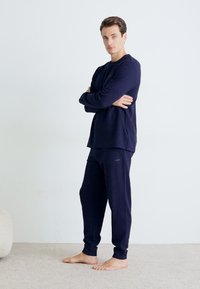 Navy Loungewear-Set aus weichem Stoff; langärmliges Oberteil mit Rundhalsausschnitt und passende Hose mit elastischen Bündchen, texturiertem Finish, minimalem Branding.