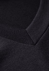 Svart tröja med en texturerad yta och V-ringad design. Har ribbad trim vid halslinningen och subtila sömnadsdetaljer.