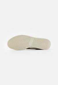 Gummisåle med zigzag mønster, kremfarge med beige aksent. Har merkevaren logo synlig på mellomsålen.