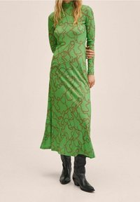 Grünes langärmliges Kleid mit figurbetontem Schnitt, mit einem braunen Kettenmuster und einer weichen Textur, kombiniert mit schwarzen kniehohen Stiefeln.