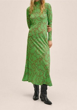 Robe longue verte à manches longues avec une silhouette cintrée, ornée d'un motif en chaîne marron et d'une texture douce, associée à des bottes noires jusqu'au genou.