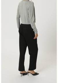 Haut argenté à manches longues et court, assorti à un pantalon noir taille haute. Des mules noires à talons complètent la tenue. Texture lisse, design minimaliste.