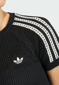 Czarny dzianinowy t-shirt z krótkim rękawem, z białym wzorem trzech pasków i małym białym logo na piersi. Teksturowana tkanina z okrągłym dekoltem.