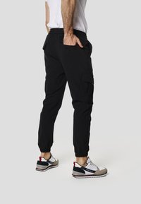 Pantalones cargo negros con puños elásticos, bolsillos laterales y un ajuste relajado, combinados con zapatillas grises y blancas con detalles en rojo.