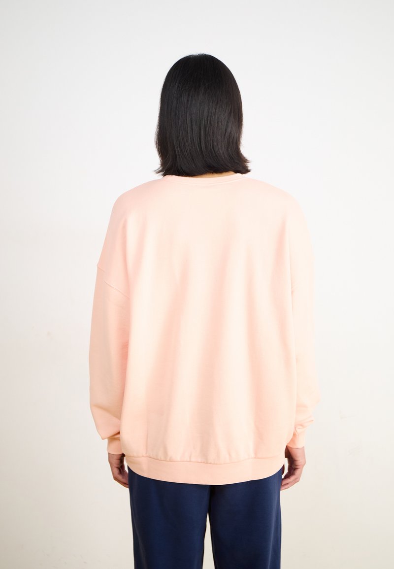 Sweat-shirt oversize rose clair avec des épaules larges, des poignets et un ourlet côtelés. Texture de tissu douce, design uni, et vue arrière montrée.