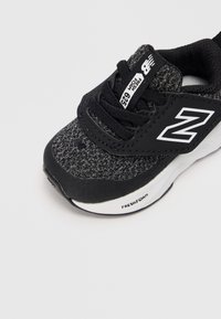 Chaussure de sport noire et grise avec un dessus texturé, un bout en caoutchouc lisse et des accents blancs. Présente un collier rembourré et des lacets pour un maintien sécurisé.